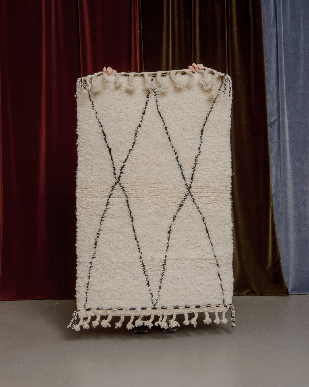 Berberlin Beniourain rug held up in front of a velvet curtain.