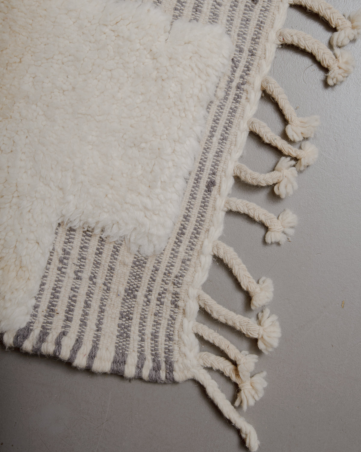 Edge of cream and grey beniourain rug with natural wool tassels along the edge.