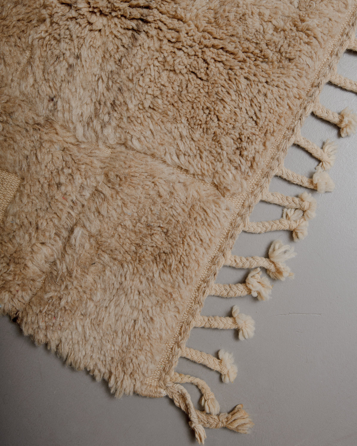 Corner of light brown beniourain rug with natural wool tassels along the edge.