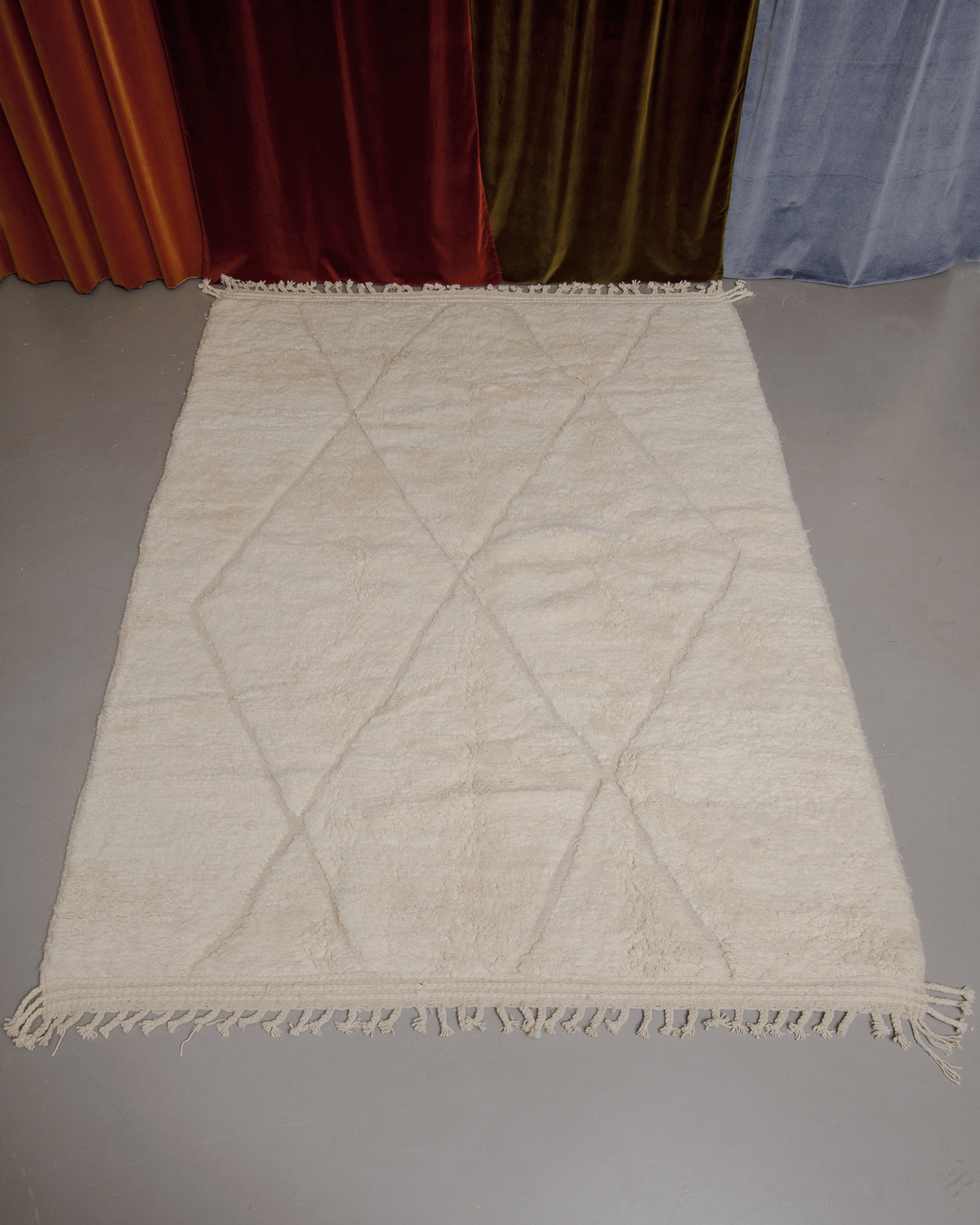 Berberlin Beniourain rug on grey floor in front of velvet curtains.