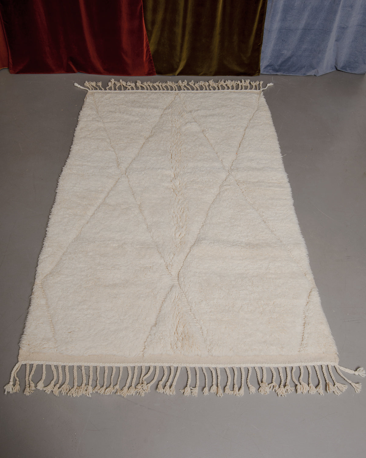 Berberlin Beniourain rug on grey floor in front of velvet curtains.