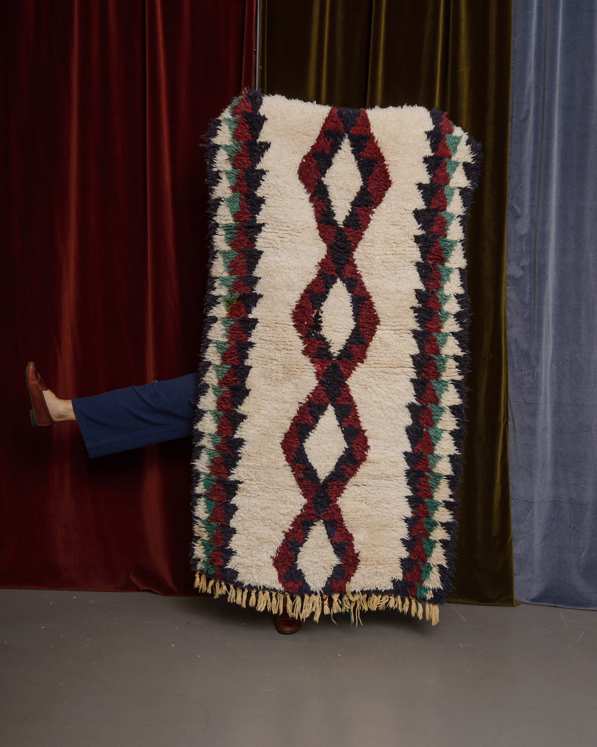 Vintage Berberlin wool runner rug being held up in front of velvet curtains.