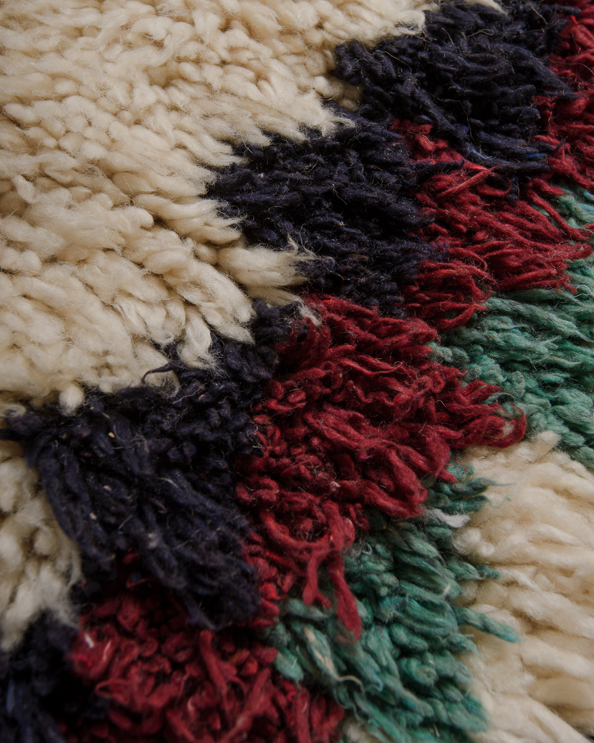 Close up of rug with cream , turquoise, navy and red wool with a shaggy texture.