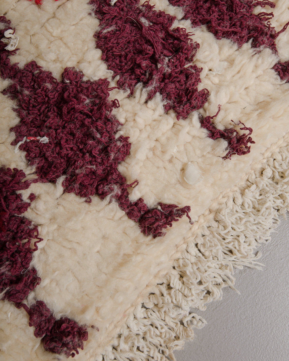 Close up of vintage rug made of cream wool and burgundy cotton with a fluffy, shaggy texture and cream fringe.
