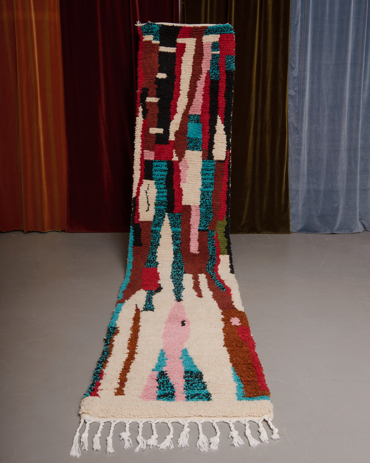 Vintage Berberlin boujaad runner rug being held up in front of a velvet curtains.