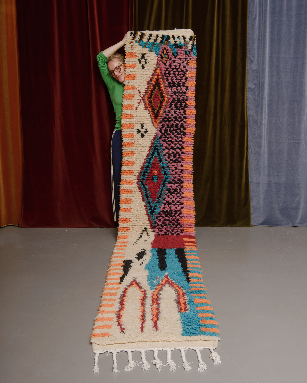 Vintage Berberlin boujaad runner rug being held up in front of a velvet curtains.