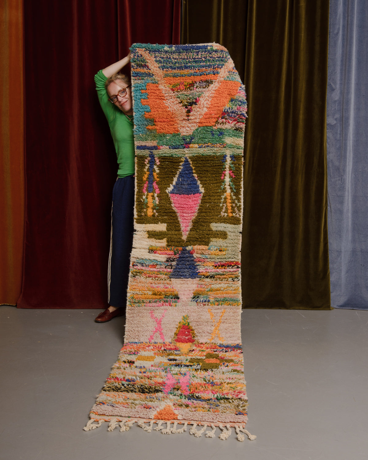 Vintage Berberlin boujaad runner rug being held up in front of a velvet curtains.