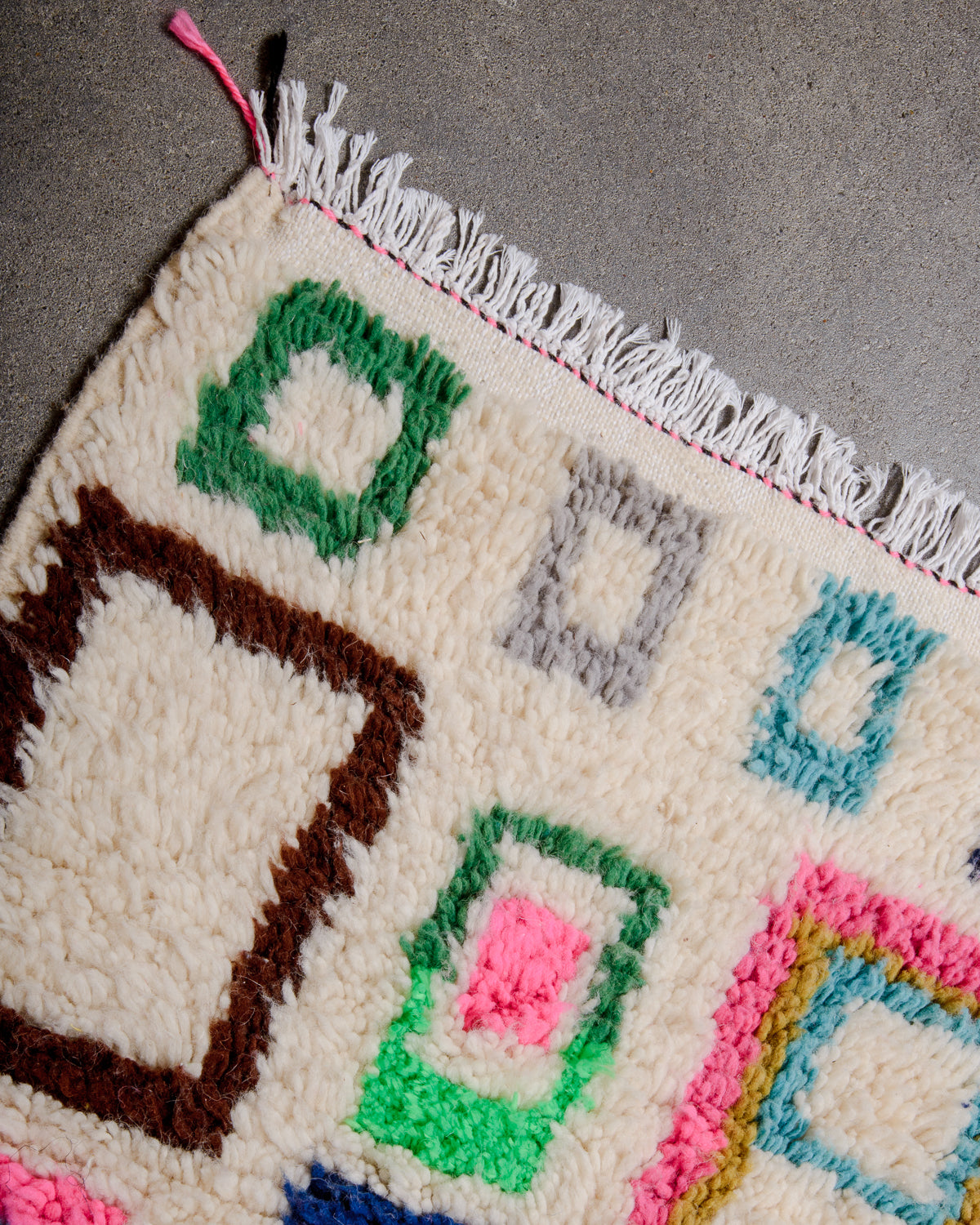 Corner of Azilal rug with white cotton tassels laying on concrete floor. 