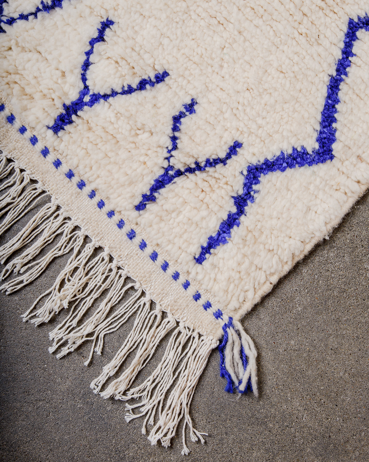 Corner of cream Azilal rug with white cotton tassels across the end.  