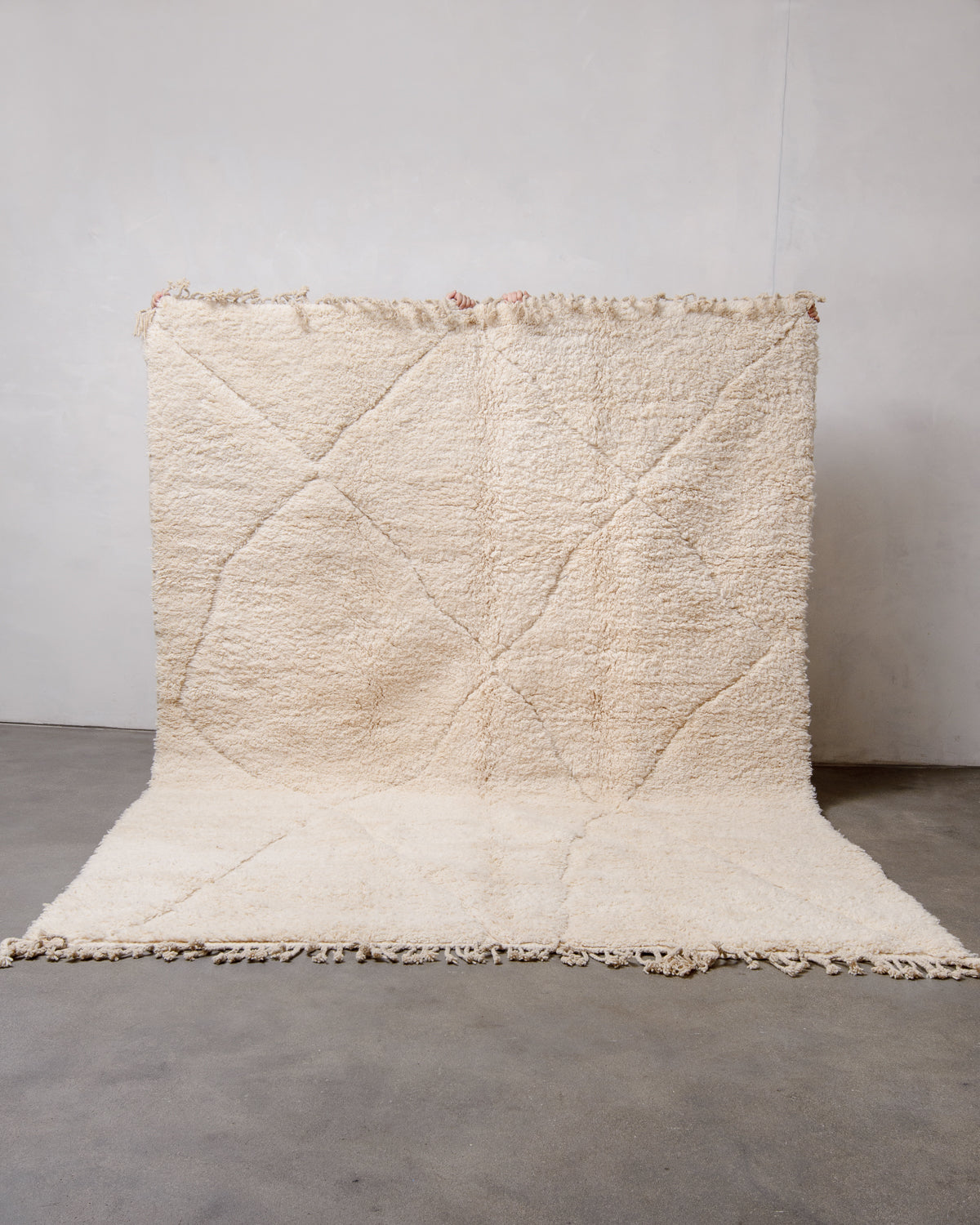 Berberlin Beniourain rug being held up in front of a white wall. 