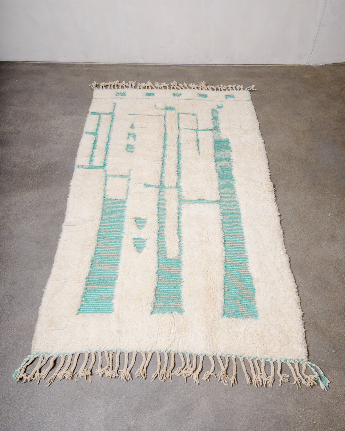 Berberlin Beniourain rug in cream and turquoise wool laying flat on a concrete floor. 