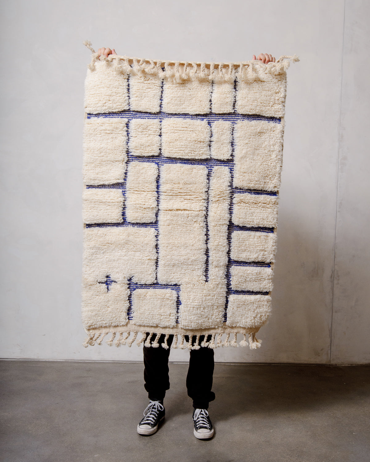 Berberlin Beniourain rug in cream and blue being held up in front of a white wall. 