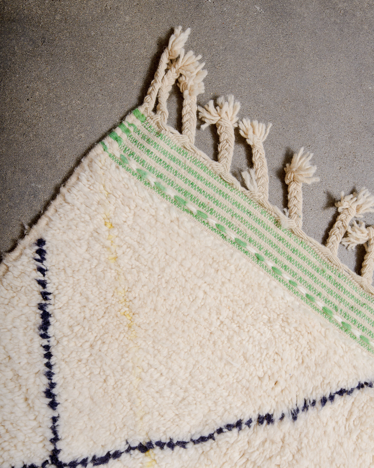Corner of Berberlin Beniourain rug with apple green striped border and natural wool tassels. 