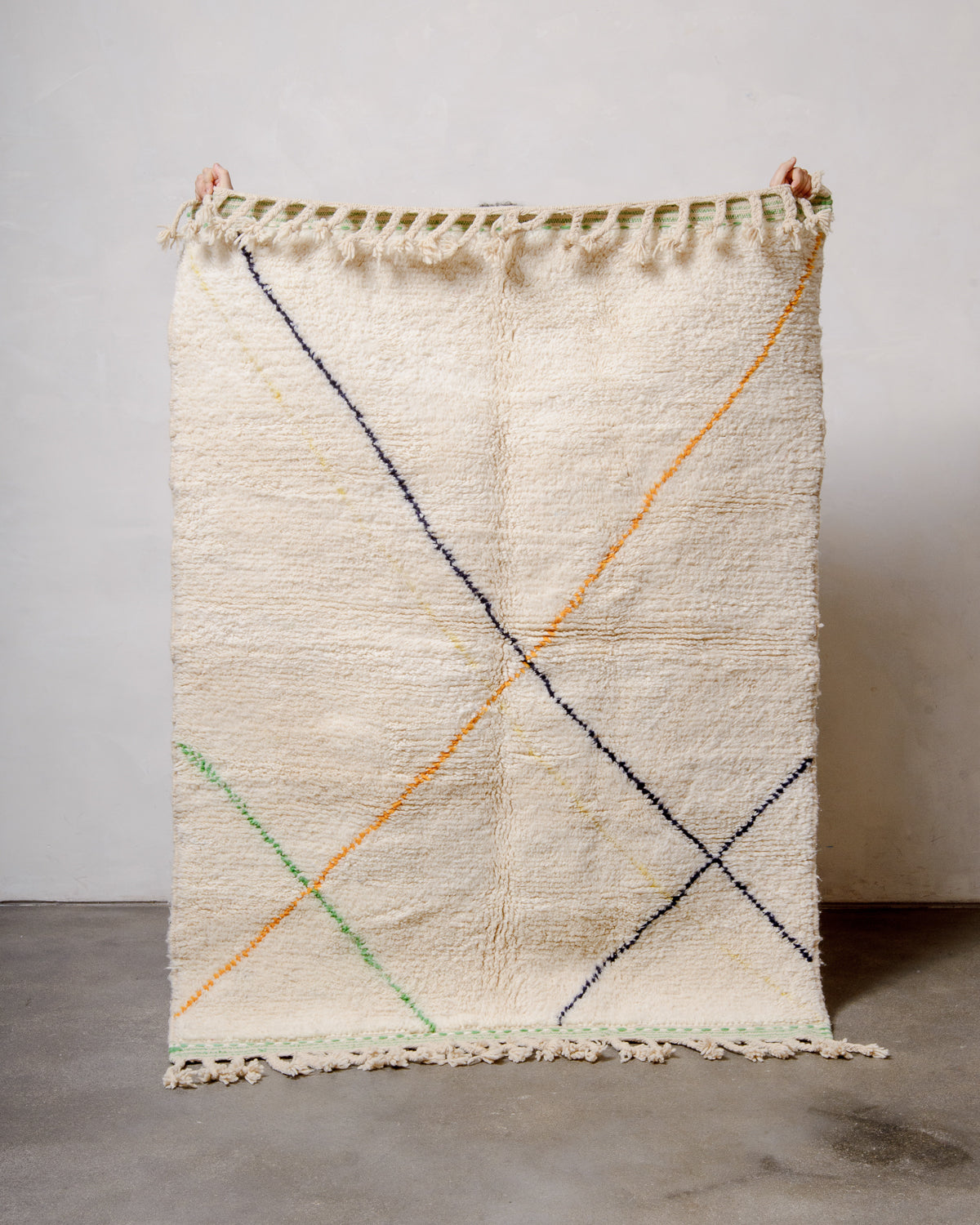 Berberlin Special Edition Beniourain rug with coloured lines being held up against white studio wall.