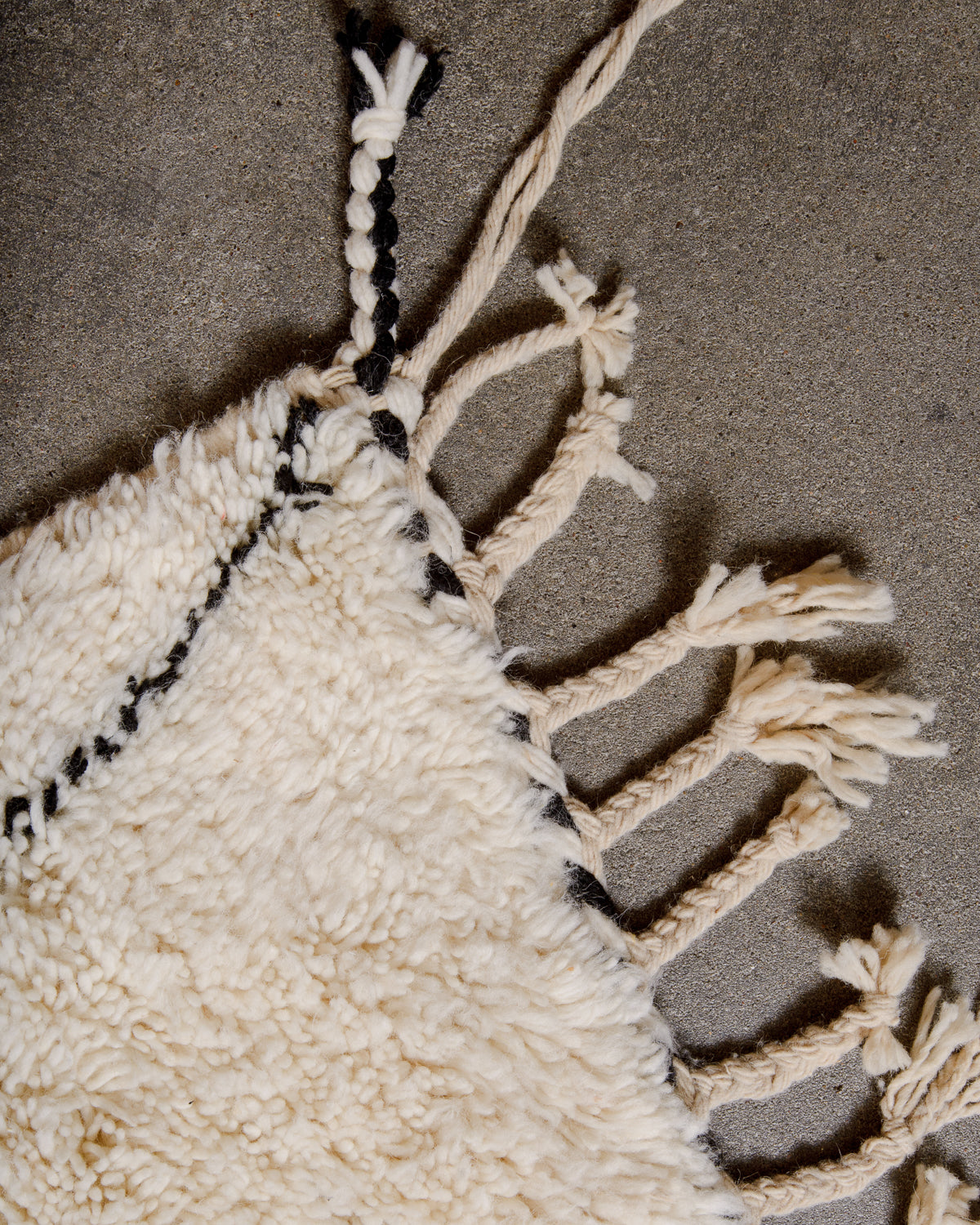 Corner of cream Beniourain rug with black diamond design and natural wool tassels. 