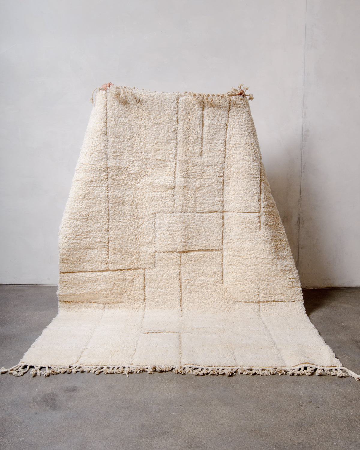 Berberlin Beniourain rug made of cream wool with minimal line design being held up in front of white wall. 