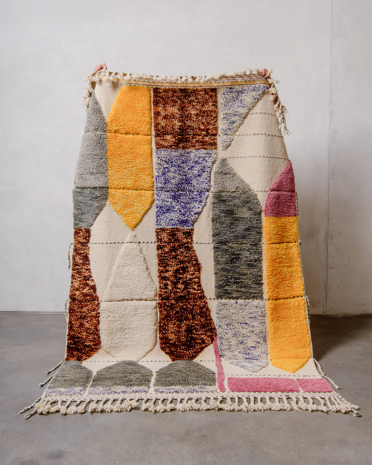 Unique Berberlin Beniourain rug with woven and knotted areas, being held up in front of a white wall. 