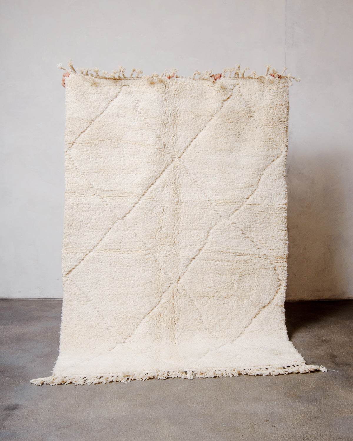 Berberlin Beniourain rug made of cream wool with a grid pattern of diamonds, being held up in front of a white wall. 