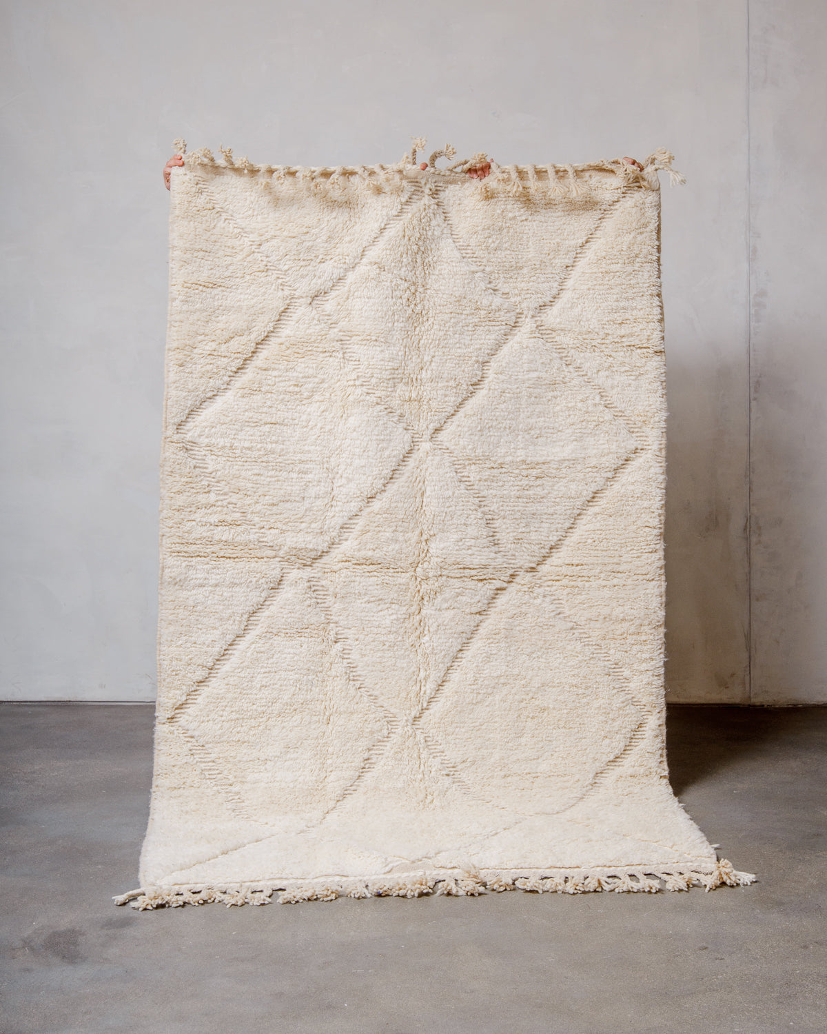 Berberlin Beniourain rug made of cream wool with a grid pattern of diamonds, being held up in front of a white wall. 