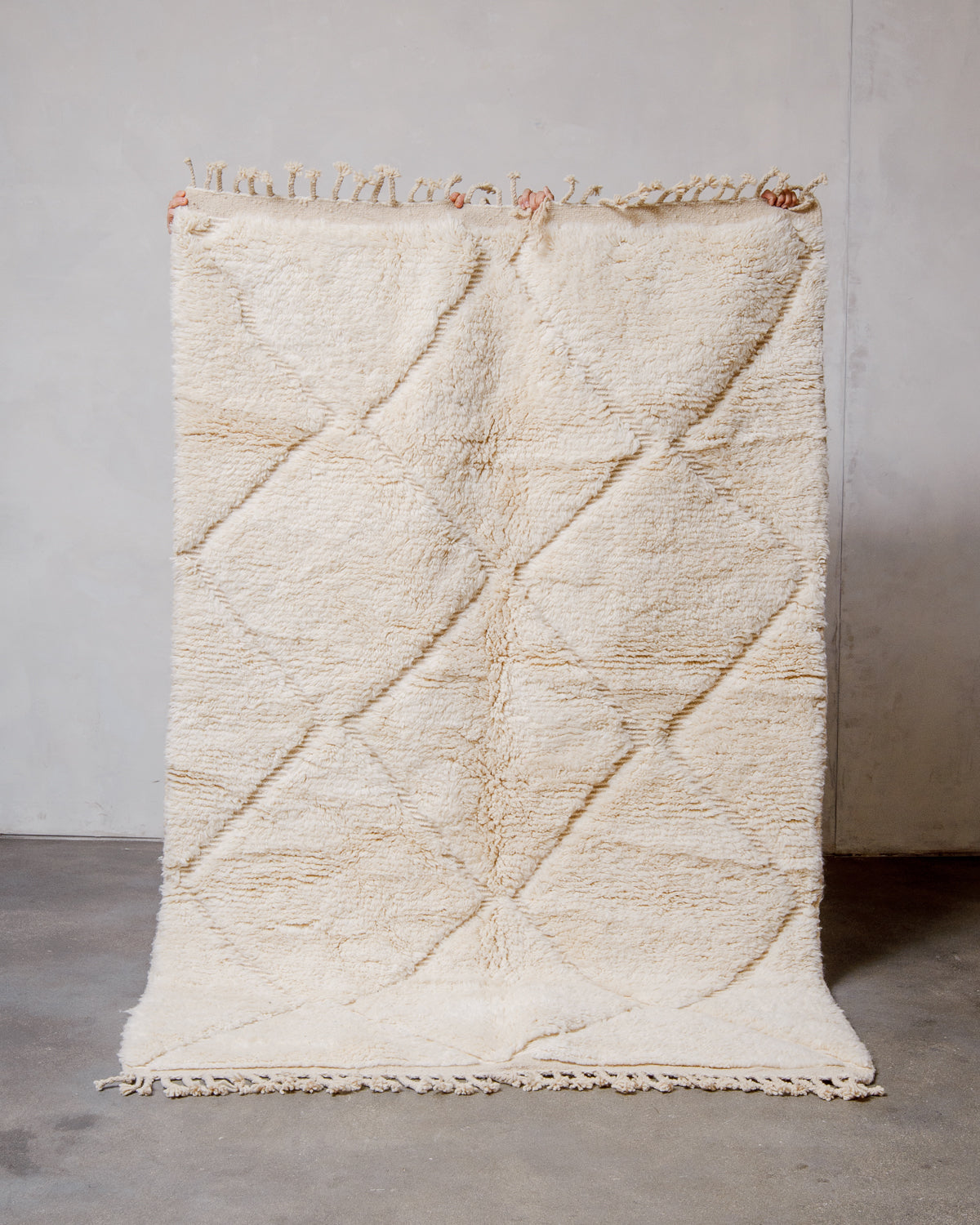 Berberlin Beniourain rug made of cream wool, being held up in front of a white wall. 