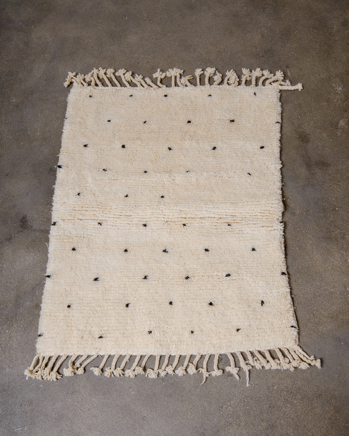Berberlin Beniourain rug with black dots laying flat on concrete studio floor. 