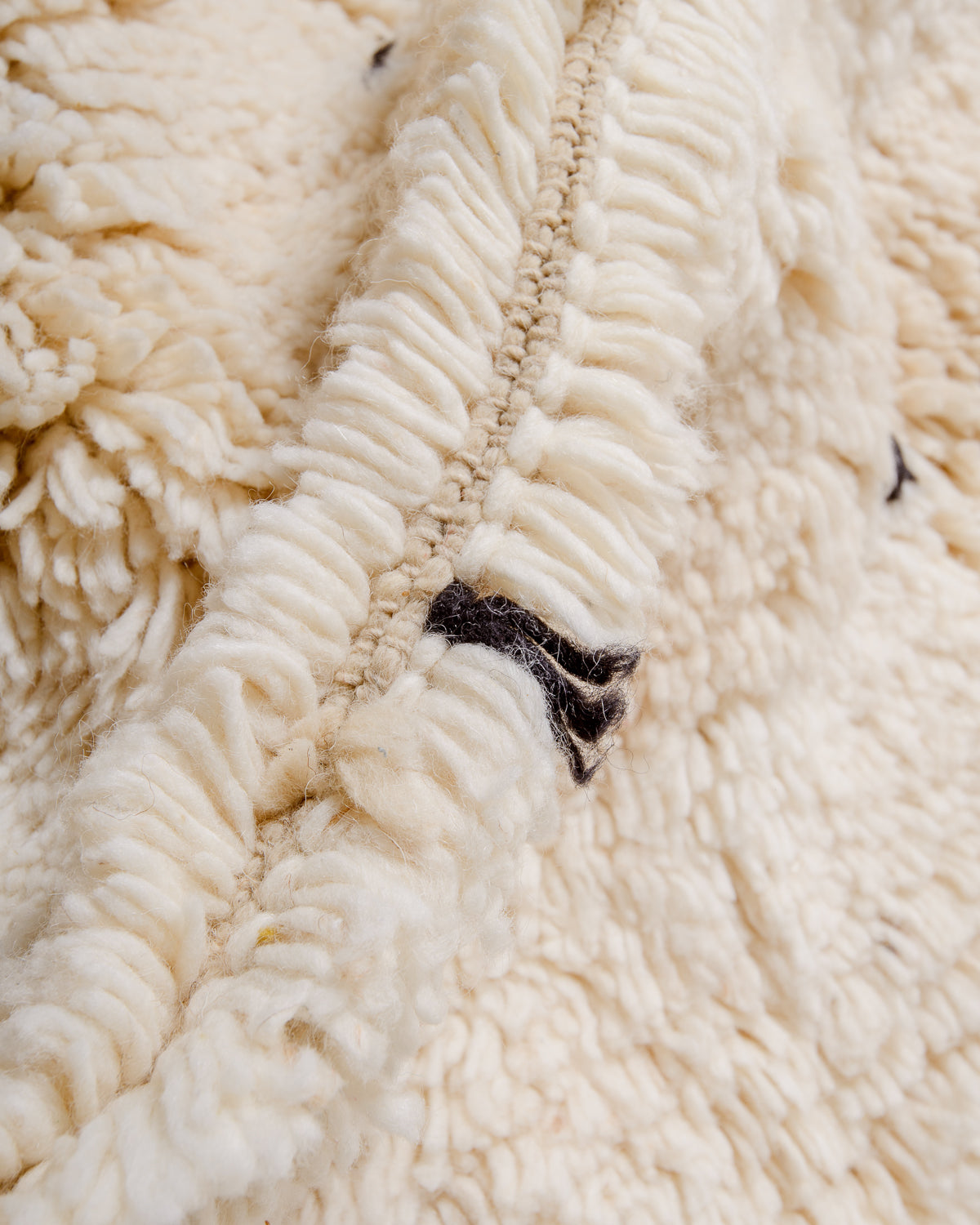 Detail of cream wool rug showing the density of the wool and black strands that make up the polka dots. 