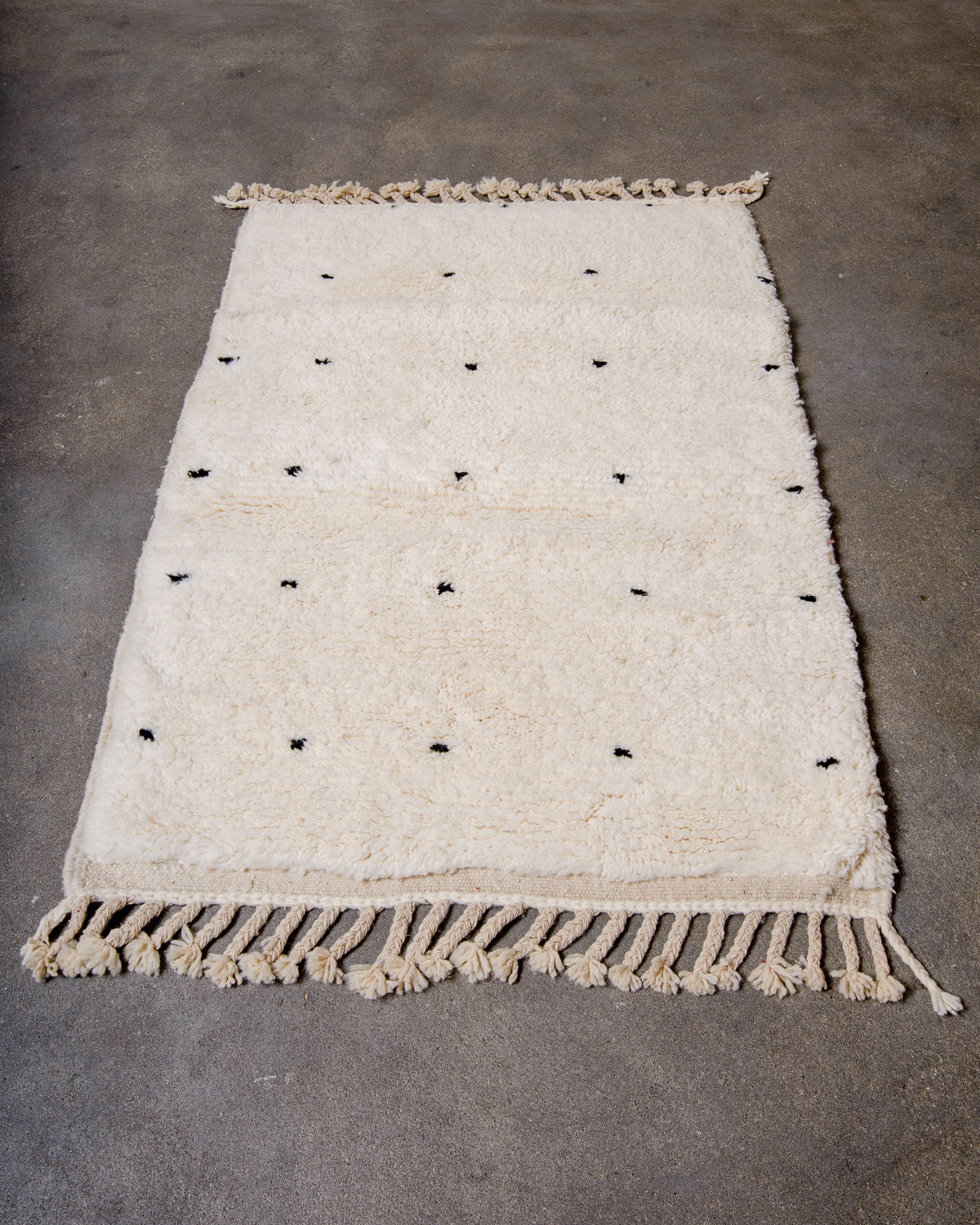 Beniourain rug in cream with black dots laying on concrete studio floor. 