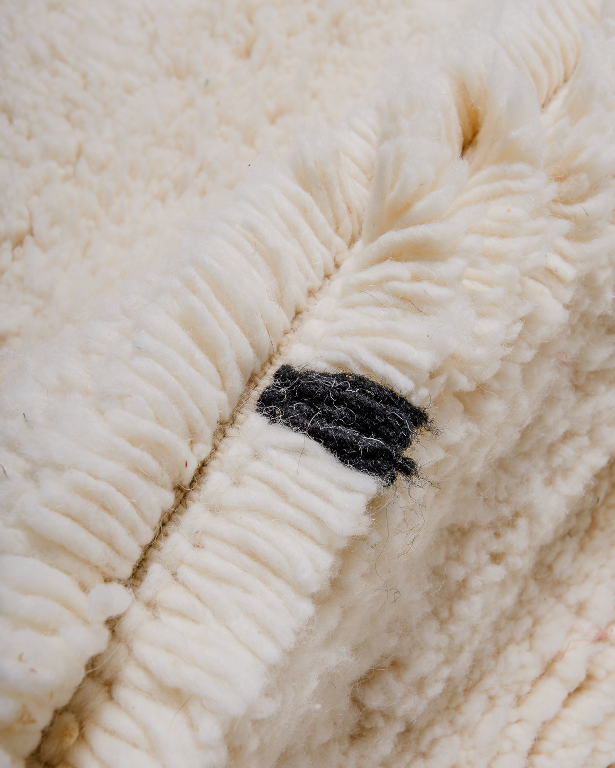 Close up of fluffy cream wool pile of Beniourain rug with black wool detail.