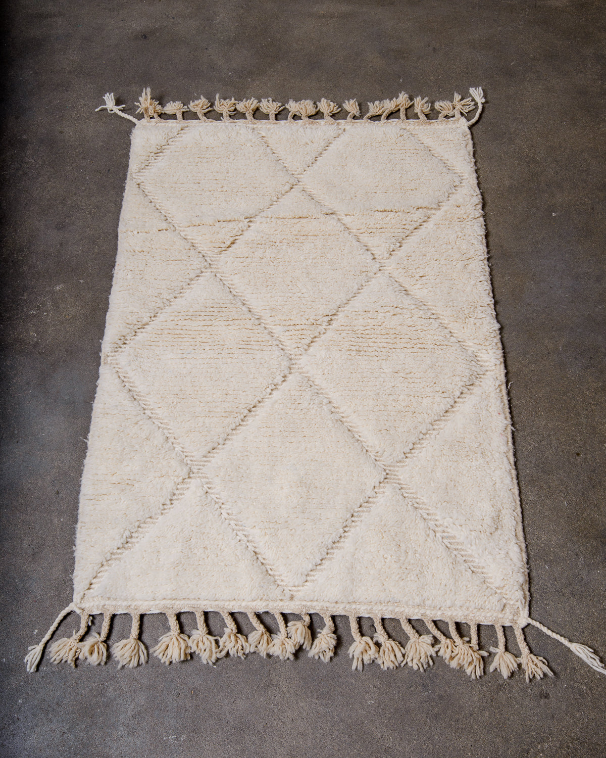 Berberlin small Beniourain rug in cream wool with woven diamond design, laying flat on concrete floor. 