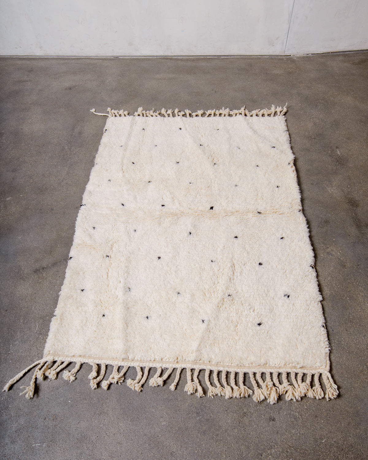 Beniourain rug in cream with black dots laying on concrete studio floor. 