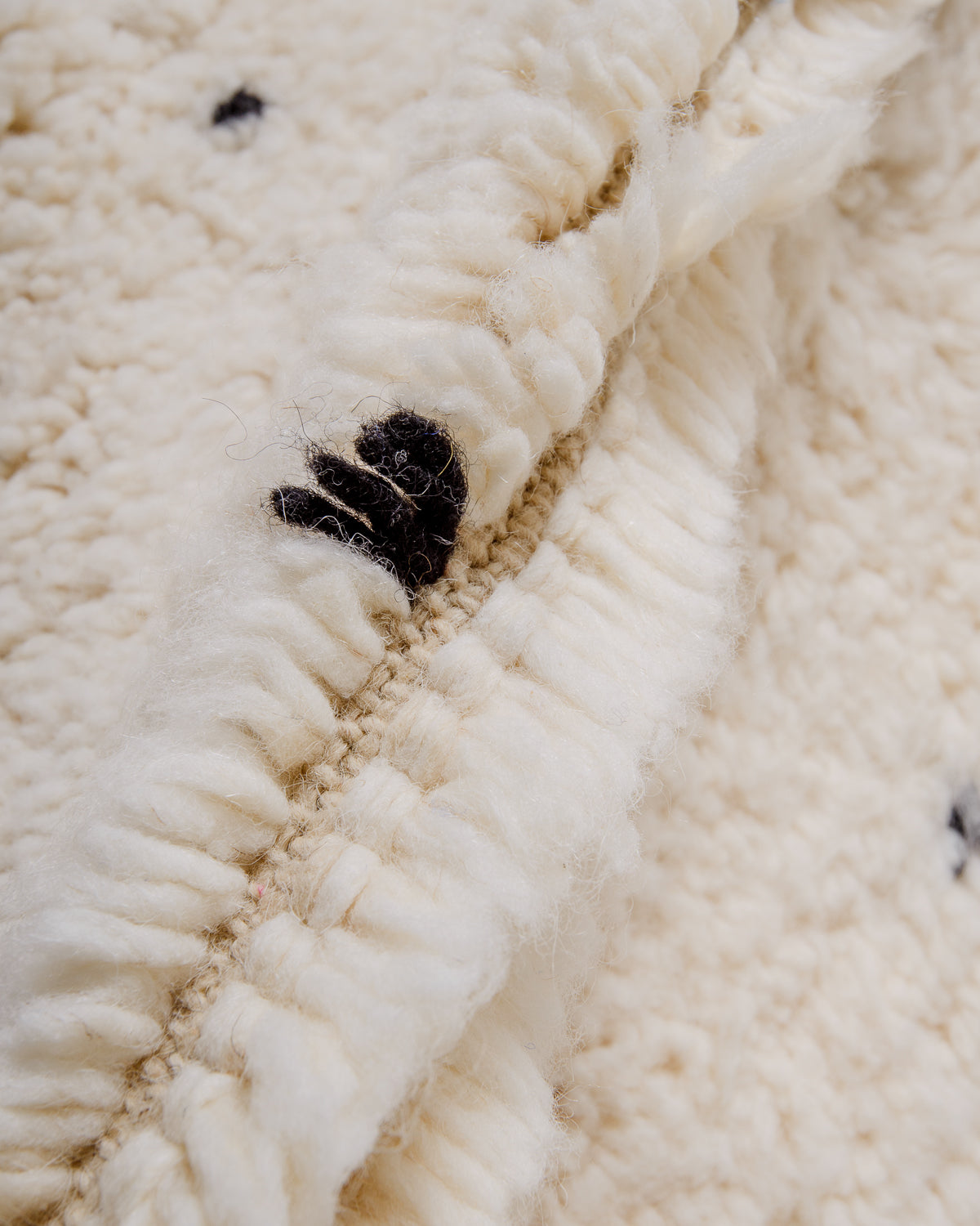 Close up of fluffy cream wool pile of Beniourain rug with black wool detail.
