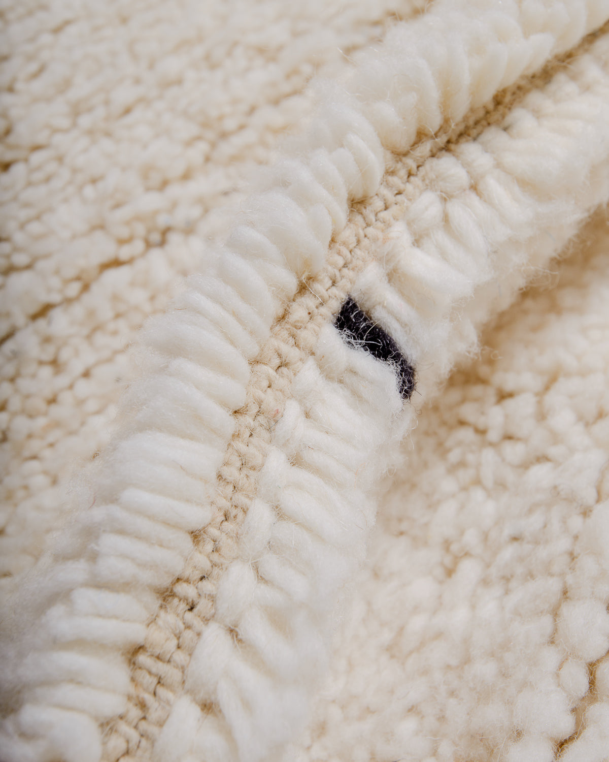 Close up of fluffy cream wool pile of Beniourain rug with black wool detail.