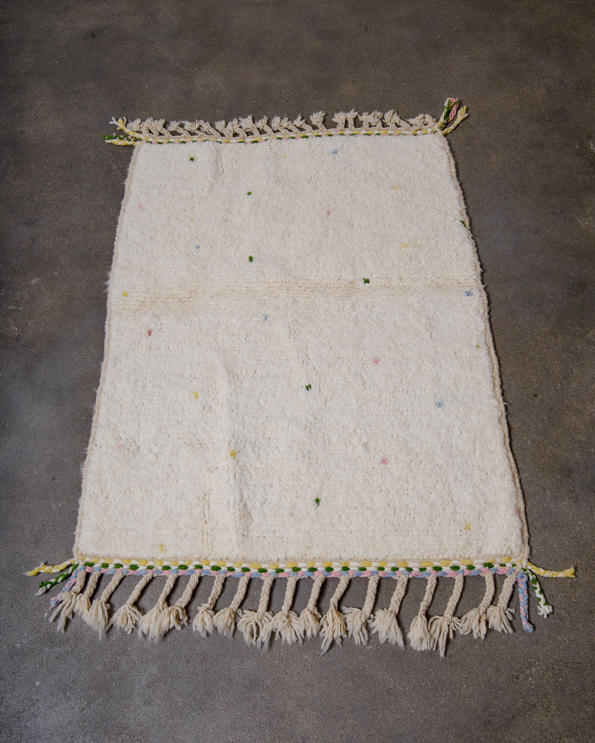 Beniourain rug in cream with coloured dots and colourful weaving on the ends laying on concrete studio floor. 