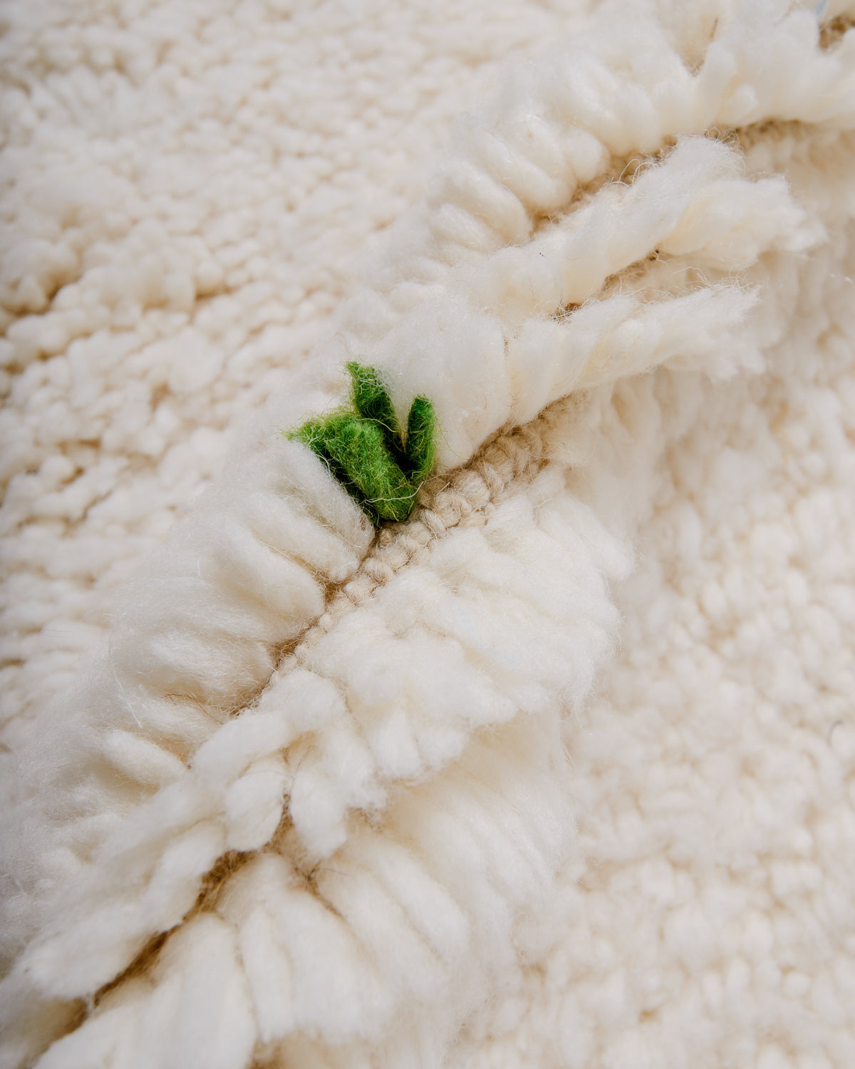 Detail of fluffy cream wool pile of Beniourain rug with green wool detail.