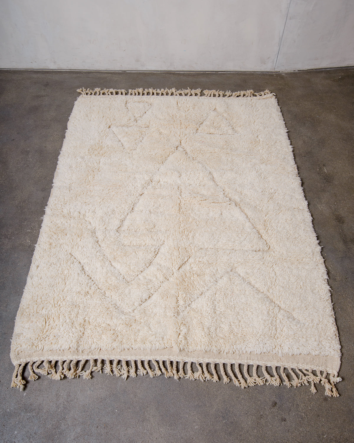 Cream wool rug with design woven in natural wool laying flat on concrete floor.