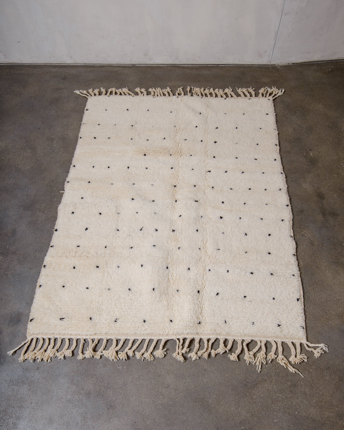 Berberlin Beniourain rug in cream wool with black dots laying on concrete floor.