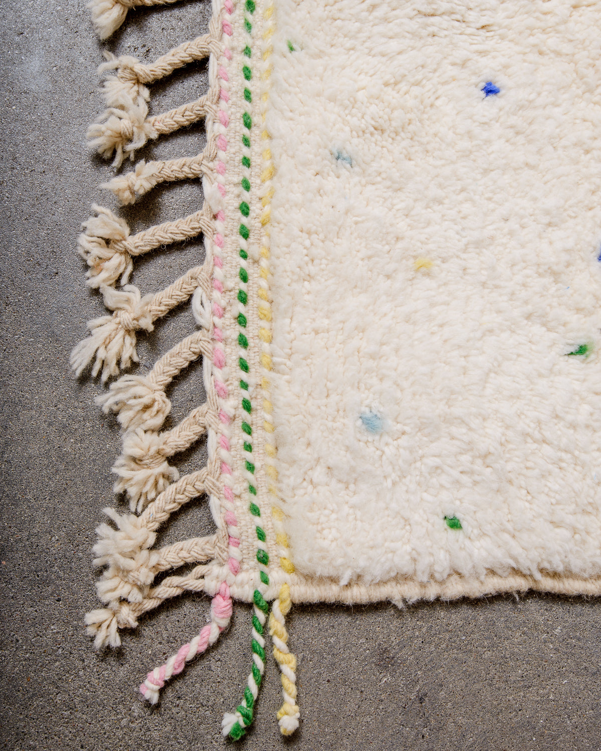 Corner of Berber rug with coloured weaving on the ends and natural wool tassels across the top. 