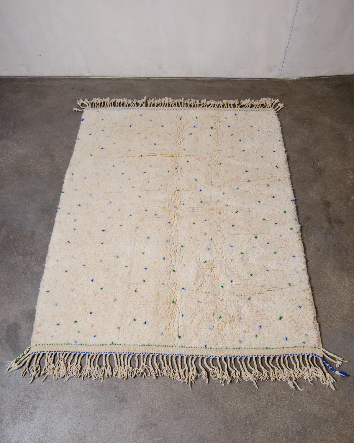 Berberlin Beniourain rug in cream wool with colourful dots laying on concrete floor.