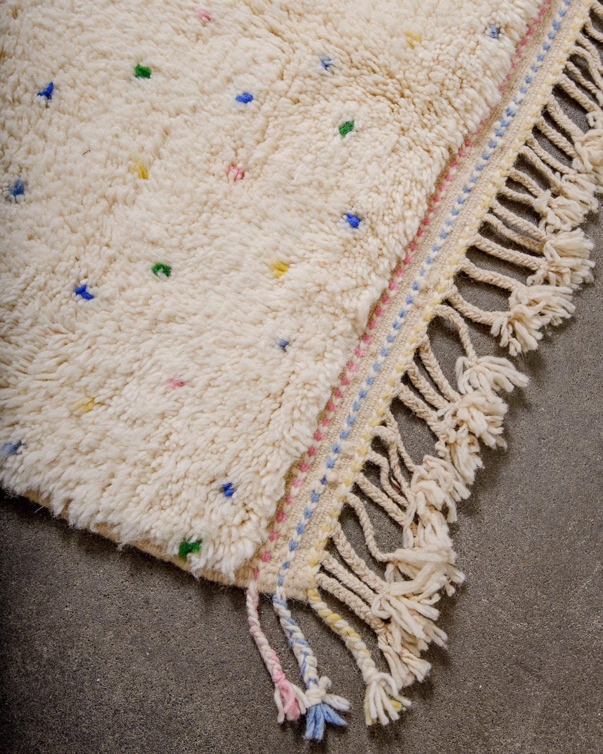 Corner of Berber rug with coloured weaving on the ends and natural wool tassels across the top. 