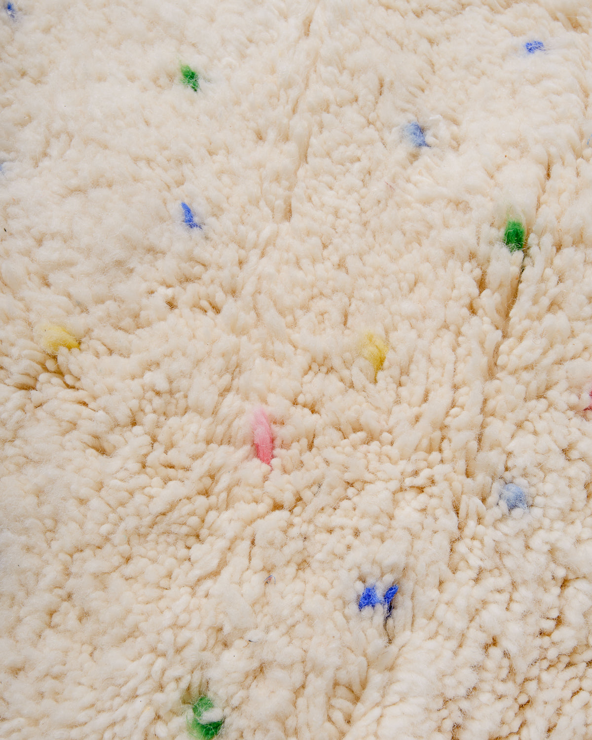 Detail of cream wool rug showing the texture of the wool and the coloured polka dots. 