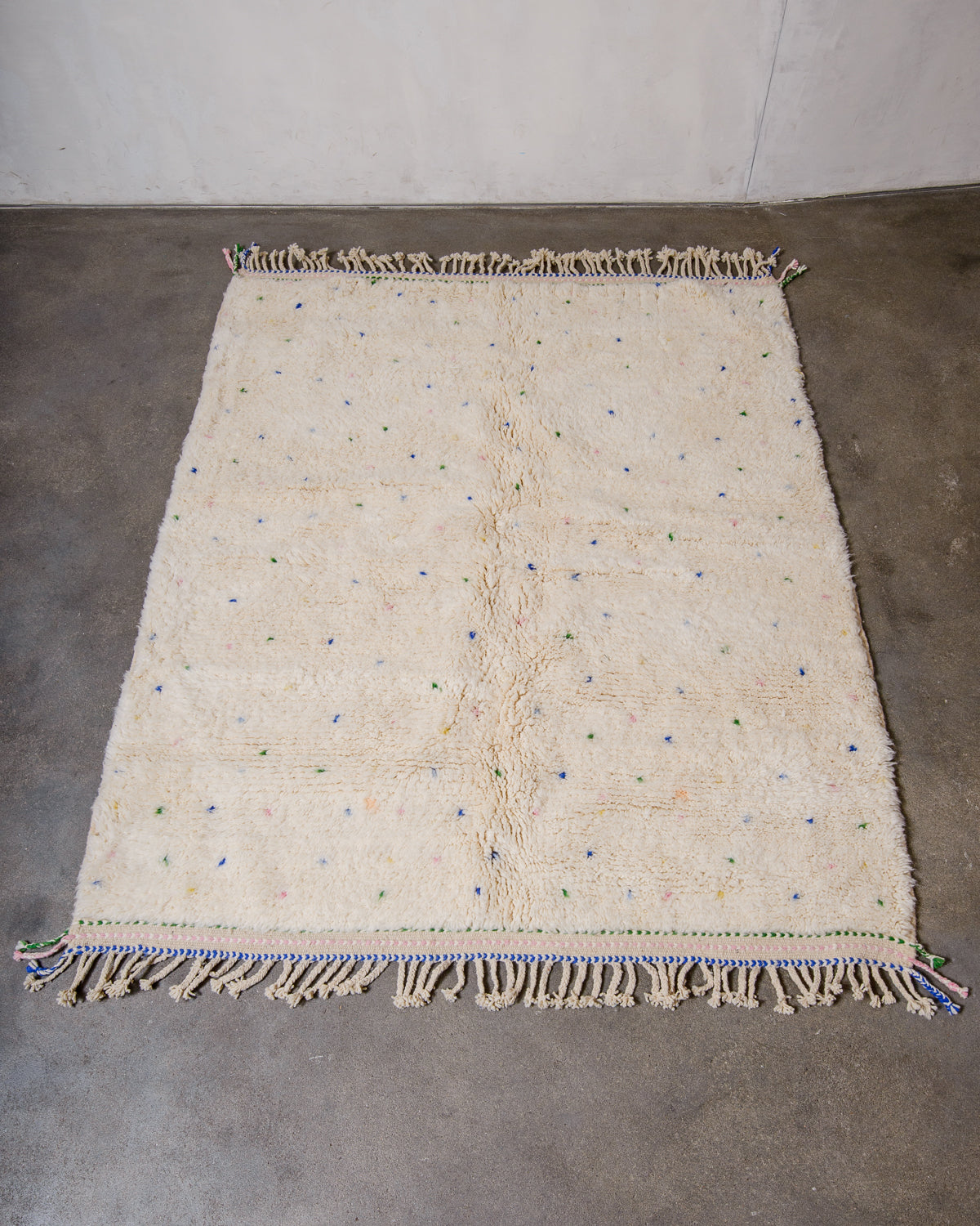 Berberlin Beniourain rug in cream wool with coloured dots laying on concrete floor.