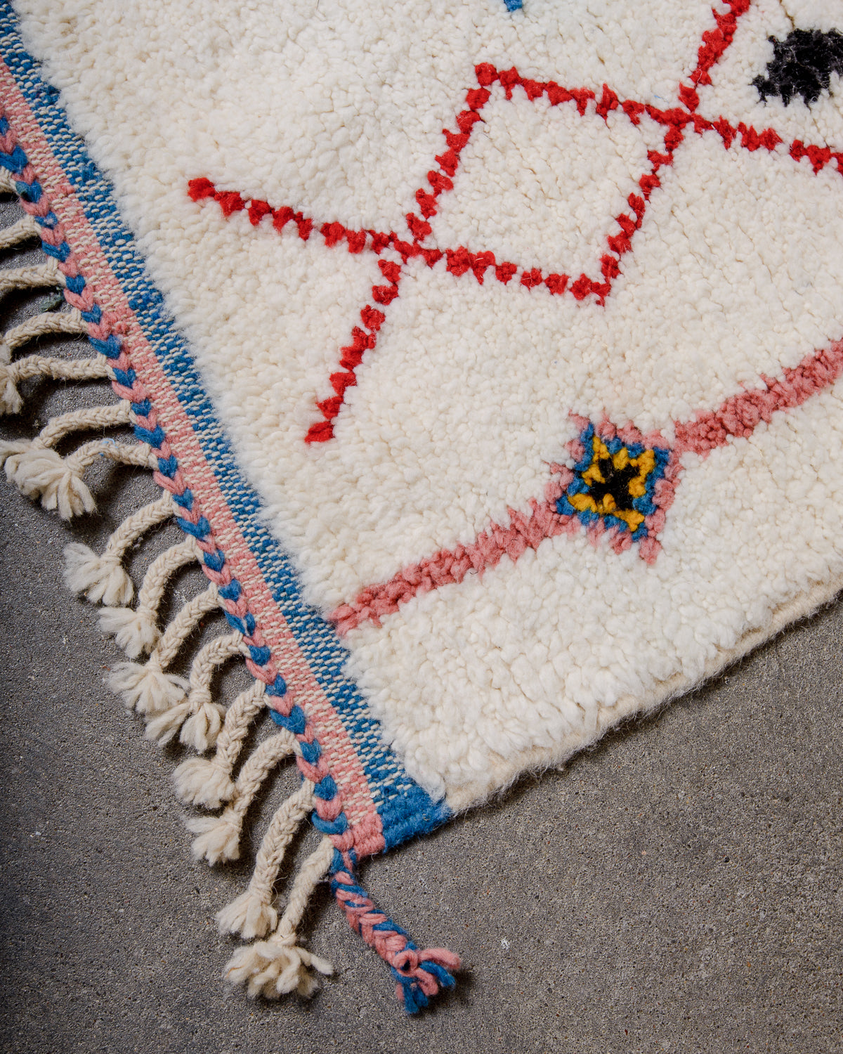Corner of beniourain rug with natural wool tassels and a tightly woven end in blue and pink wool. 