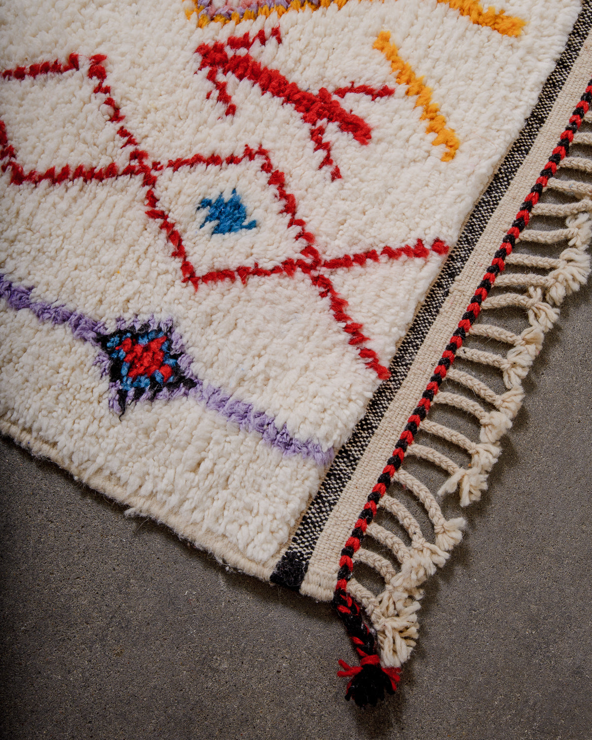Corner of beniourain rug with natural wool tassels and tightly woven end in black, red and cream wool.