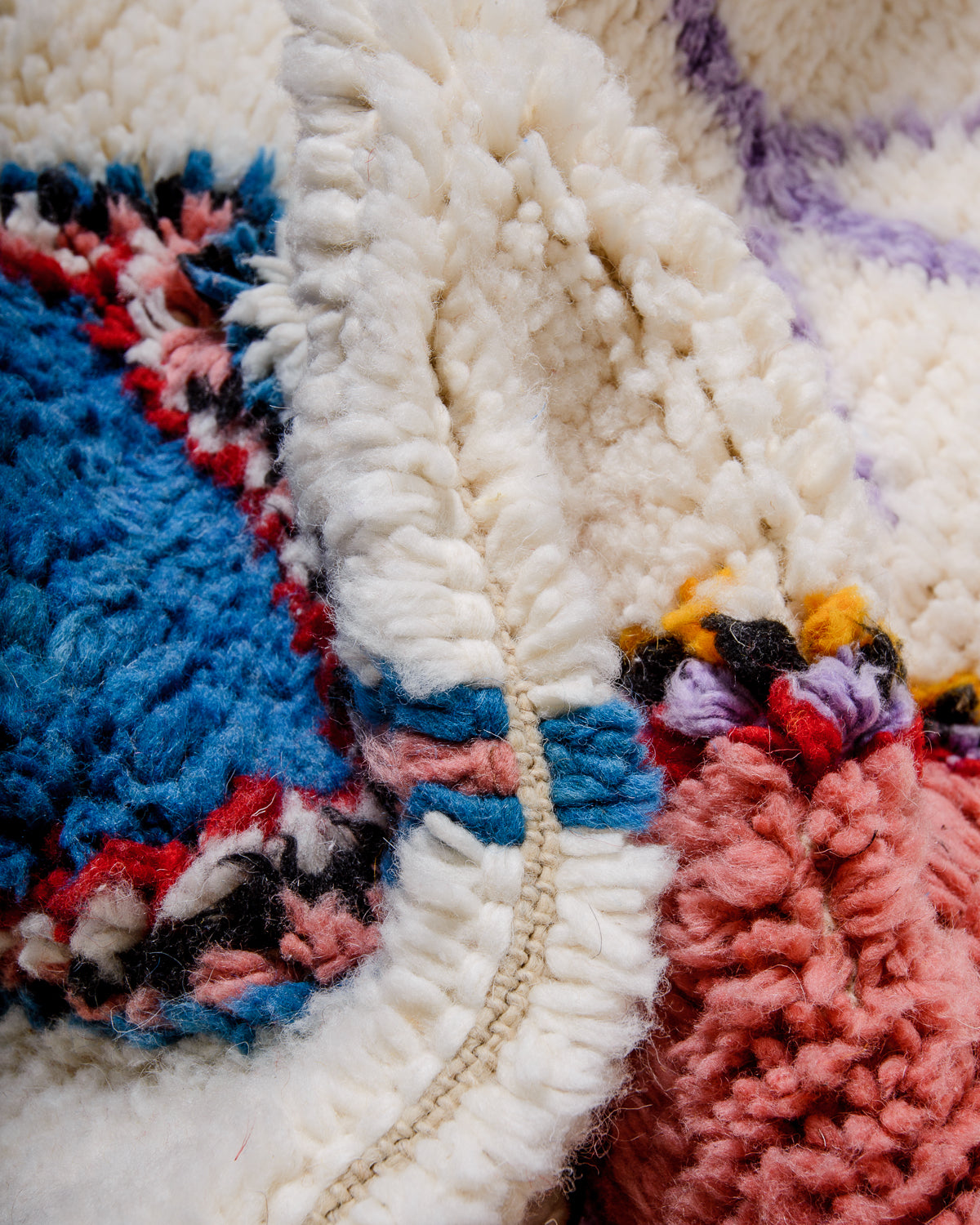Close up of knots of Beniourain rug made of fluffy wool in cream, pink, blue, coral black and yellow.