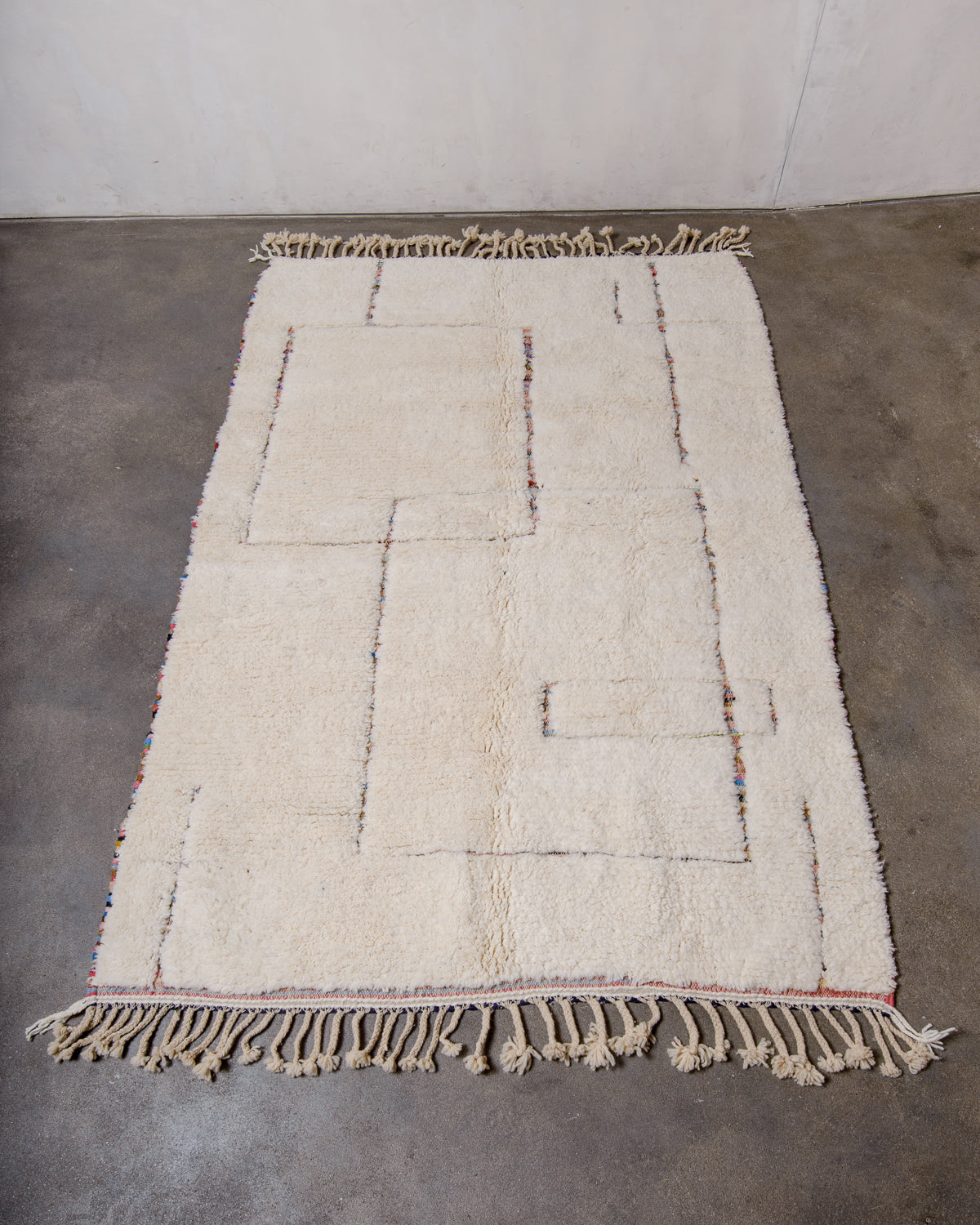 Cream wool rug with a geometric design in multi-coloured wool laying flat on a concrete floor. 