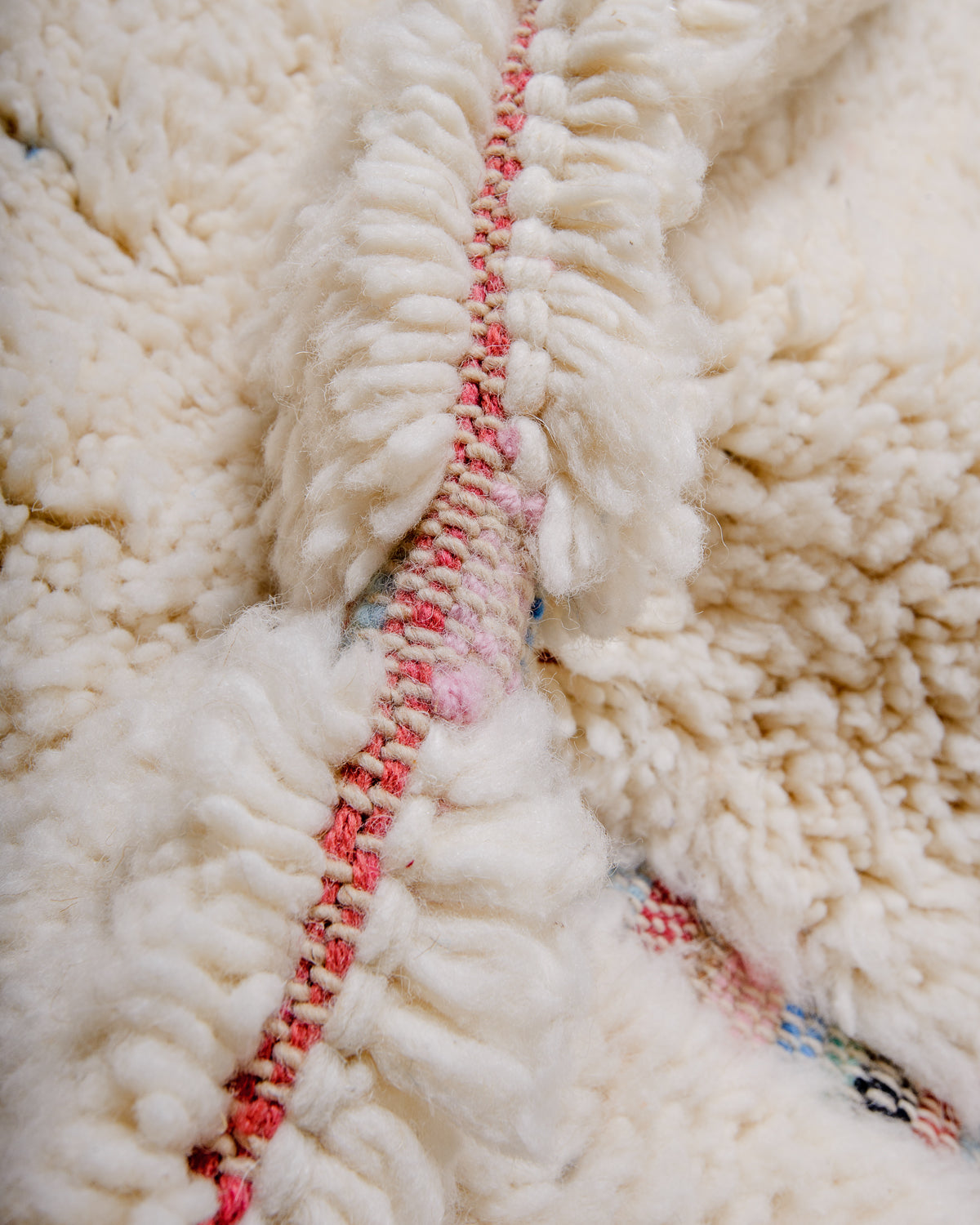Detail of rug showing colourful flat-woven design between fluffy cream wool pile. 