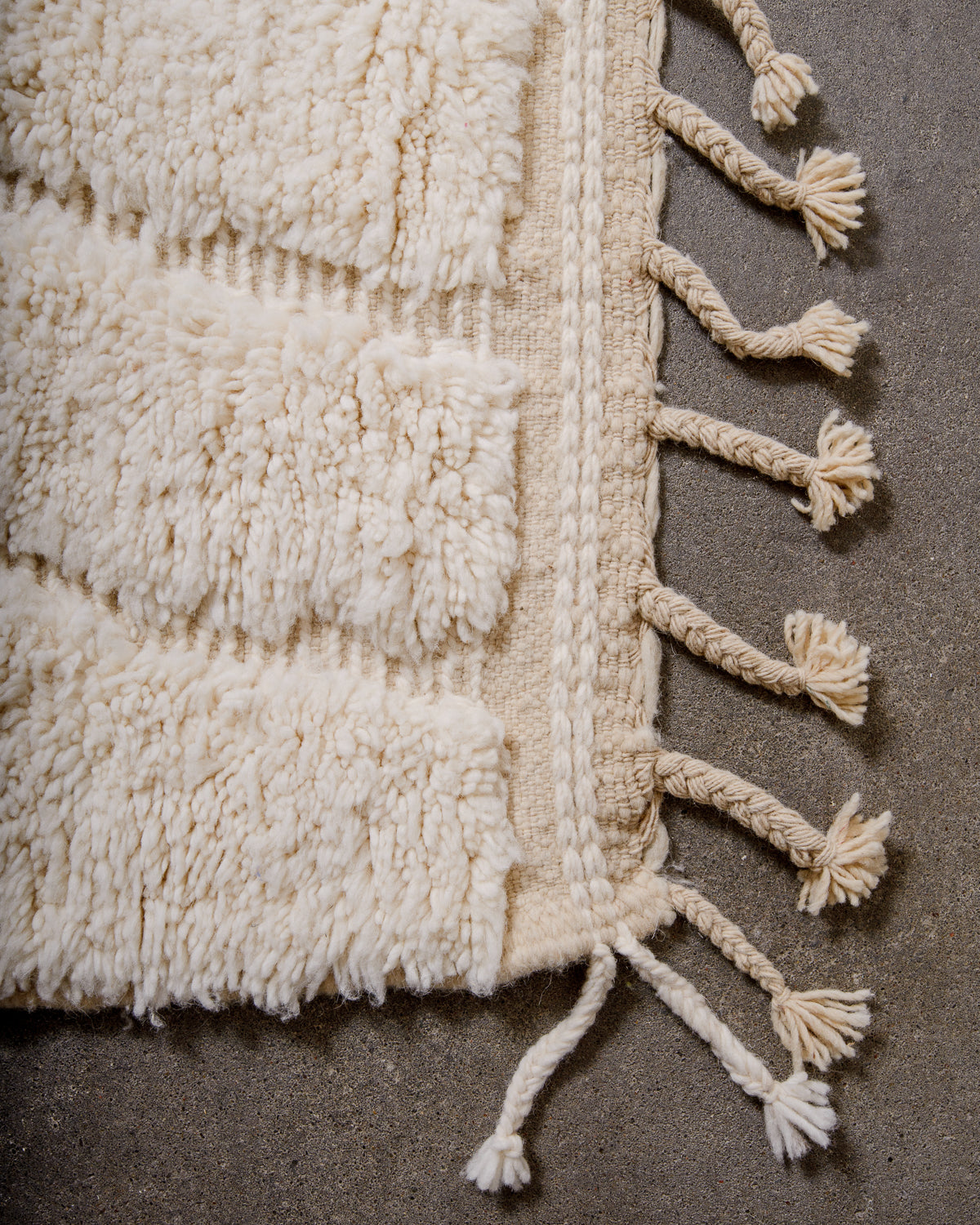 Corner of beniourain rug with tightly woven end and natural wool tassels. 