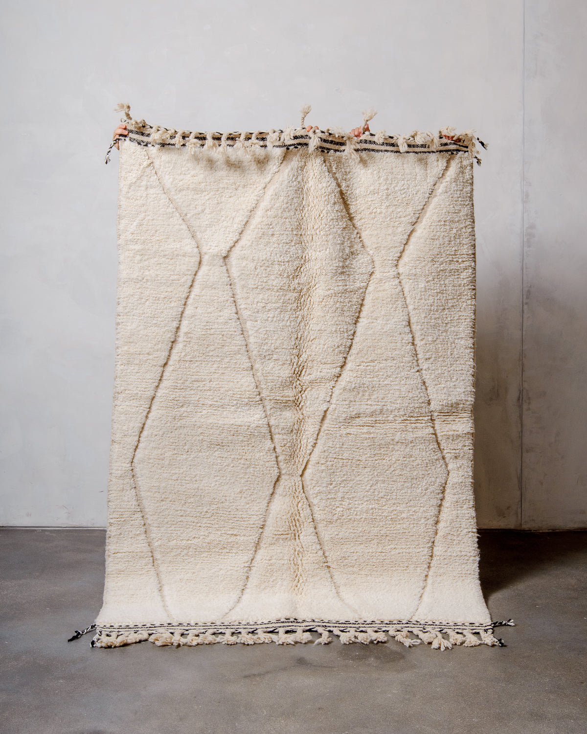 Berberlin Beniourain Rug made of cream wool being held up in front of a white wall. 