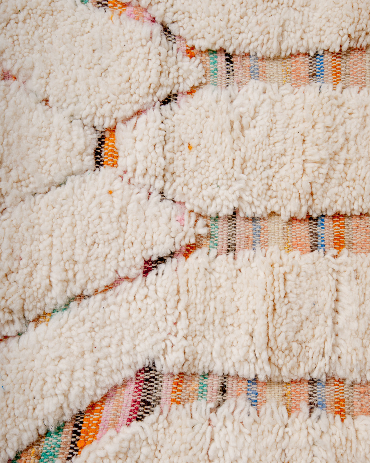 Islands of cream wool surround a striped flat-weave base in mostly warm tones with hints of blue and green. 