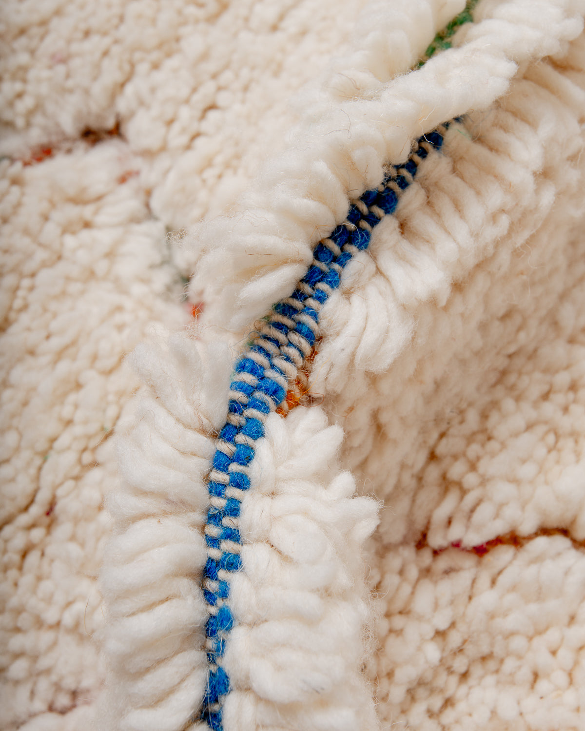 Close up of fluffy cream wool pile and colourful base of Beniourain rug.